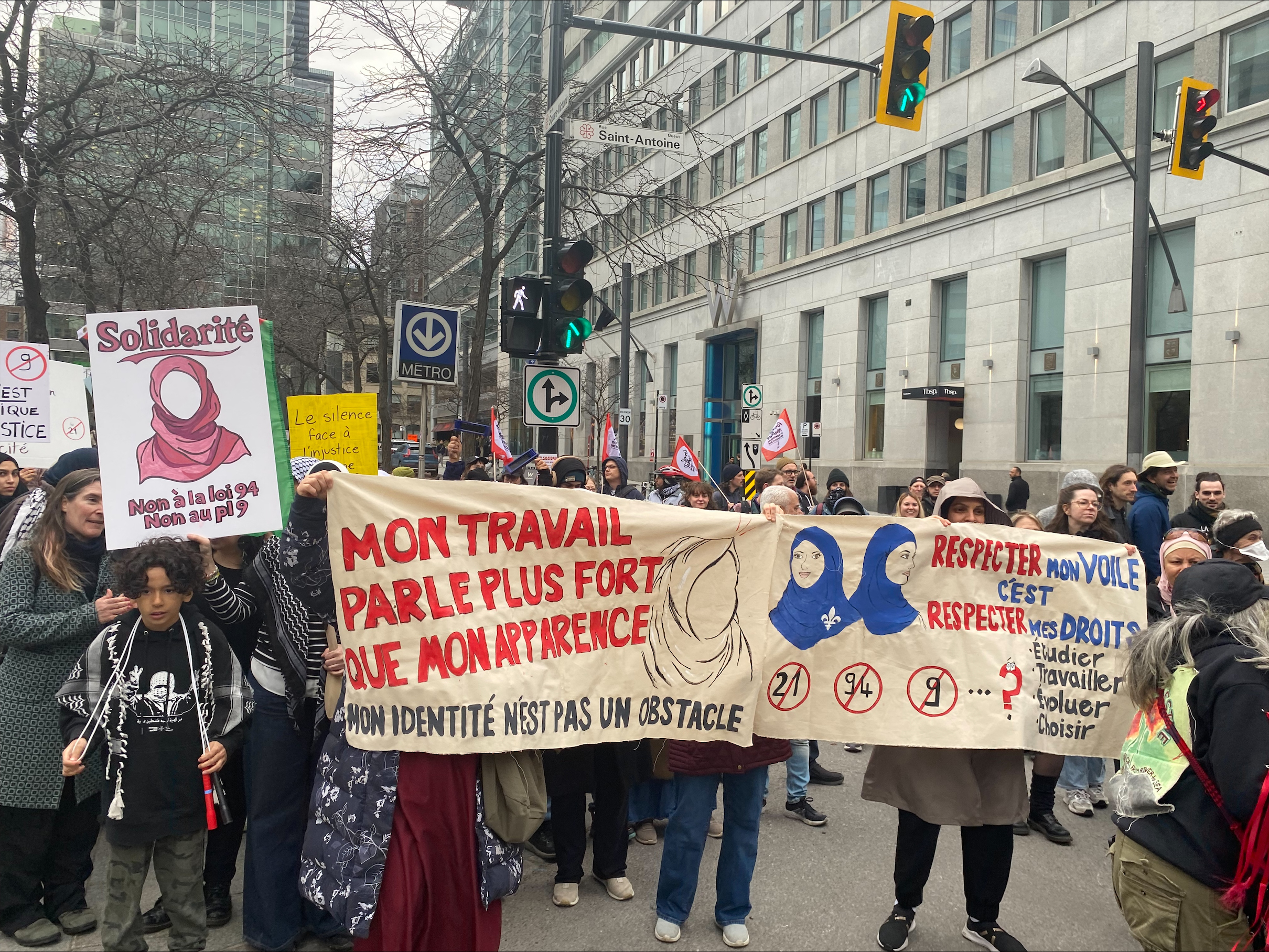 A group of people holding a banner that reads "mon travail parle plus fort que mon apparence. Mon identité n'est pas un obstacle" on the left, and reading "respecter mon voile c'est respecter mes droits: étudier, travialler, écouluer, et choisir" on the right.
